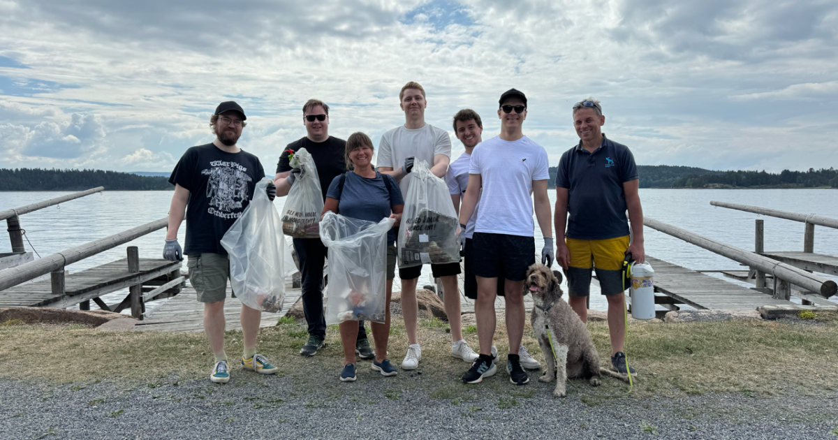 8 people and a dog standing in front of the Oslo fjord, equipped with trash bags and gloves, ready to clean the beach